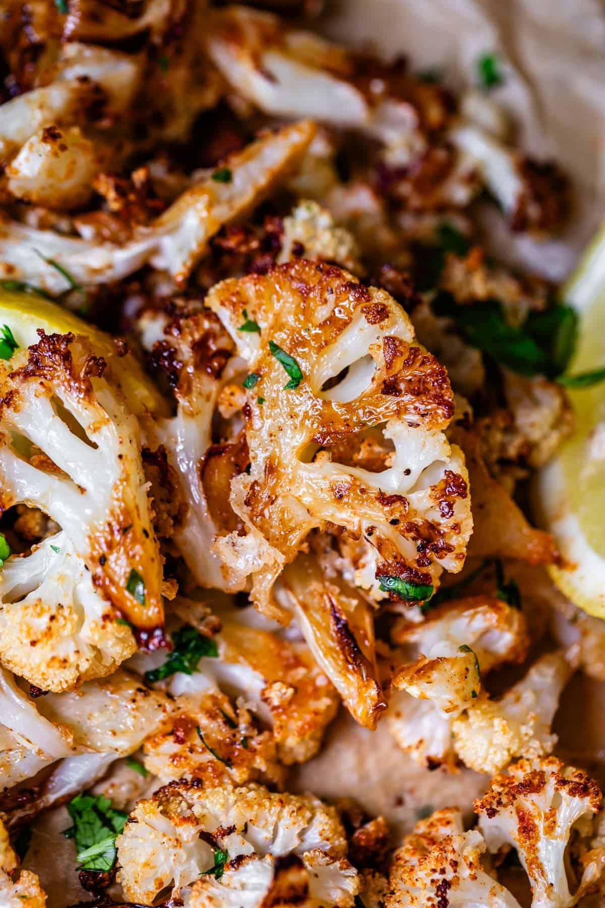 heap of roasted cauliflower with parsley and lemon garnish on parchment.