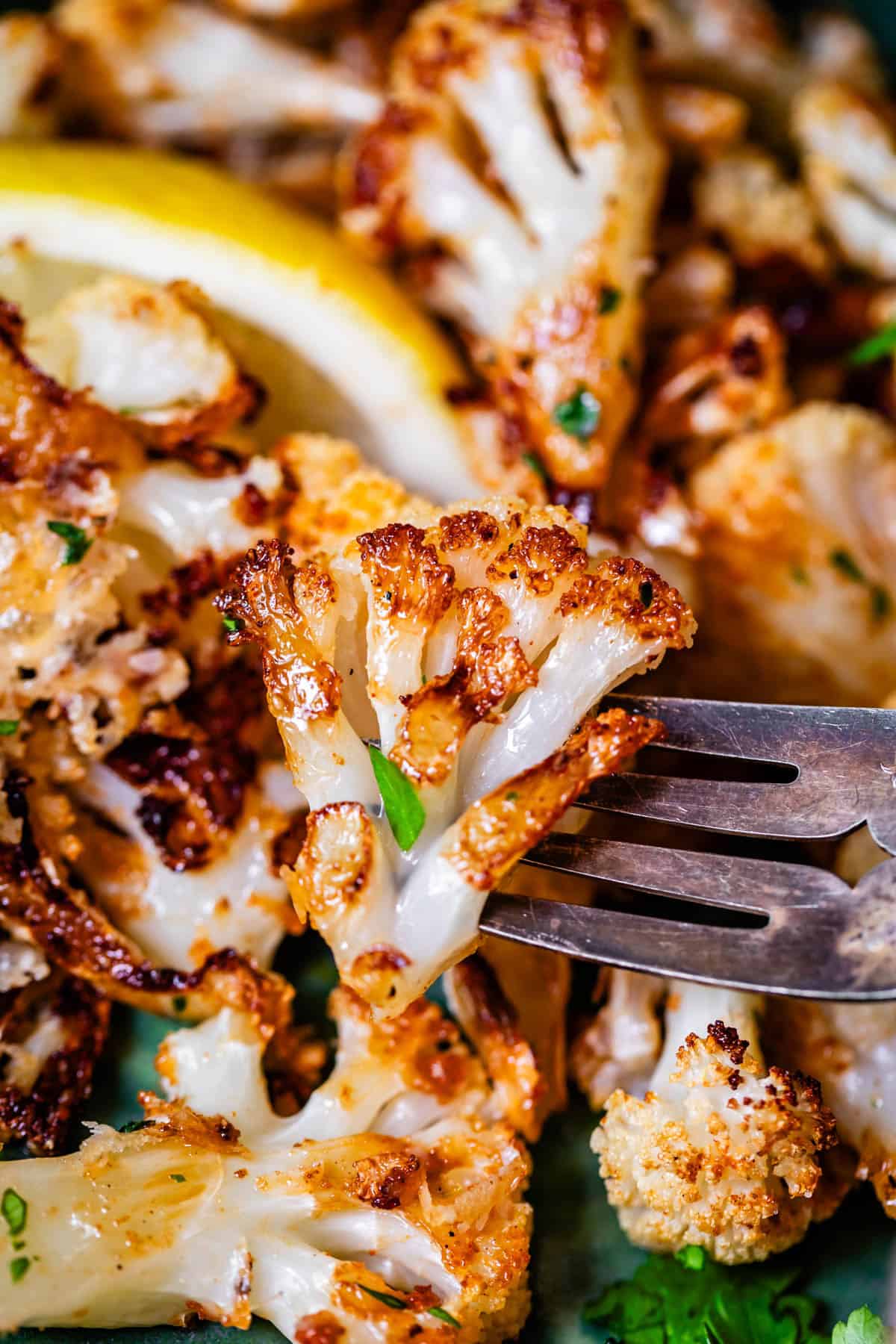 fork holding up a pierced floret of golden roasted cauliflower.