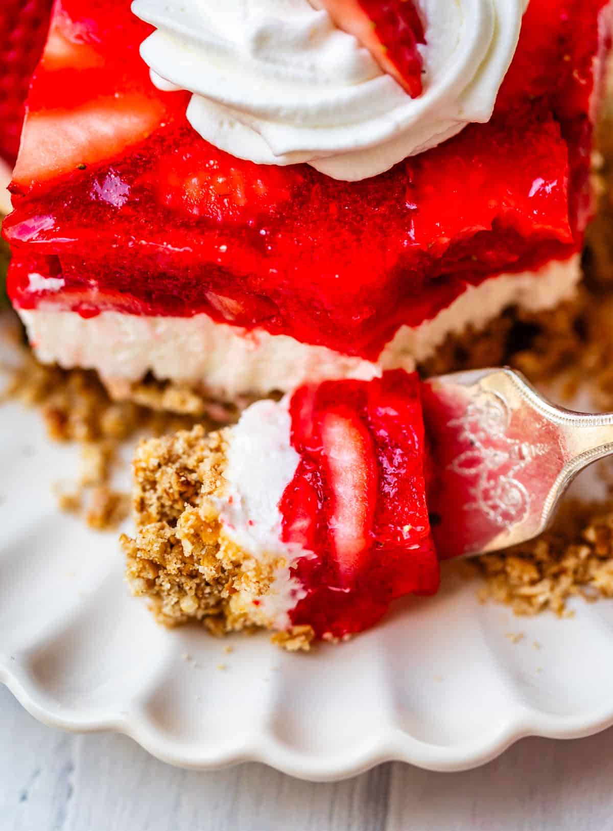 a forkful of strawberry jello pretzel salad with topping and strawberries.
