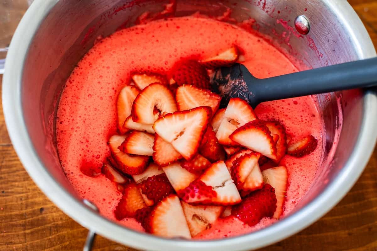 mixing strawberries into liquid jello with a spatula.