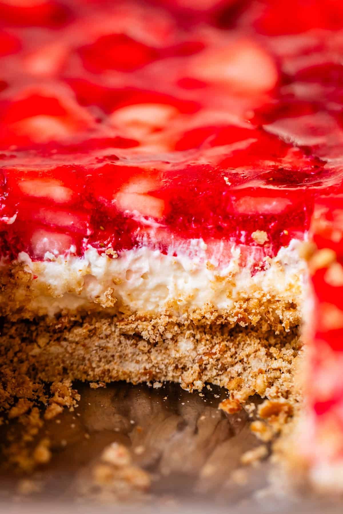 close up shot of strawberry jello pretzel salad with a slice cut out of it.