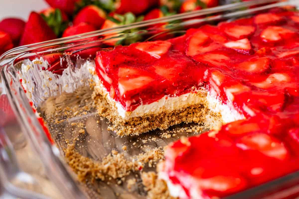 strawberry jello pretzel salad in a pan with slices cut out of it.