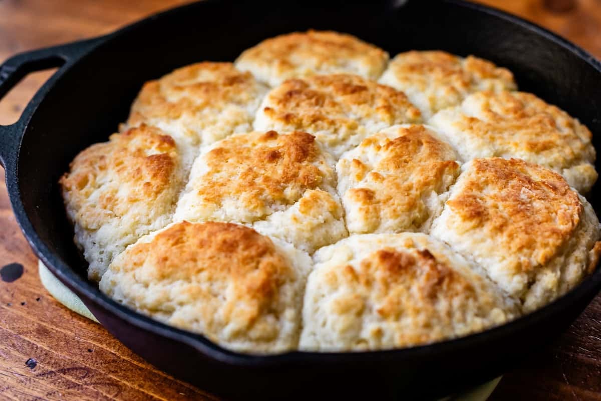 baked homemade biscuits in a cast iron skillet on a hot pad on a wood table.