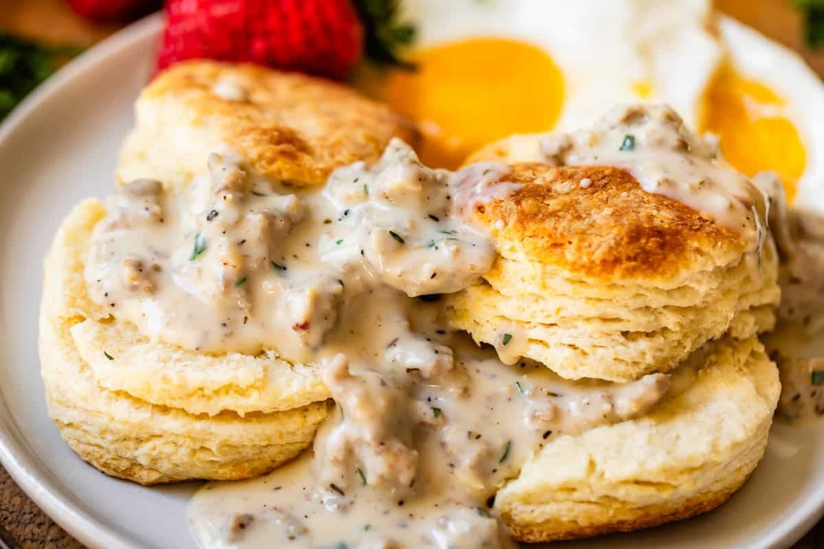 two split biscuits with the pieces stacked and sausage gravy on top and between on a plate.