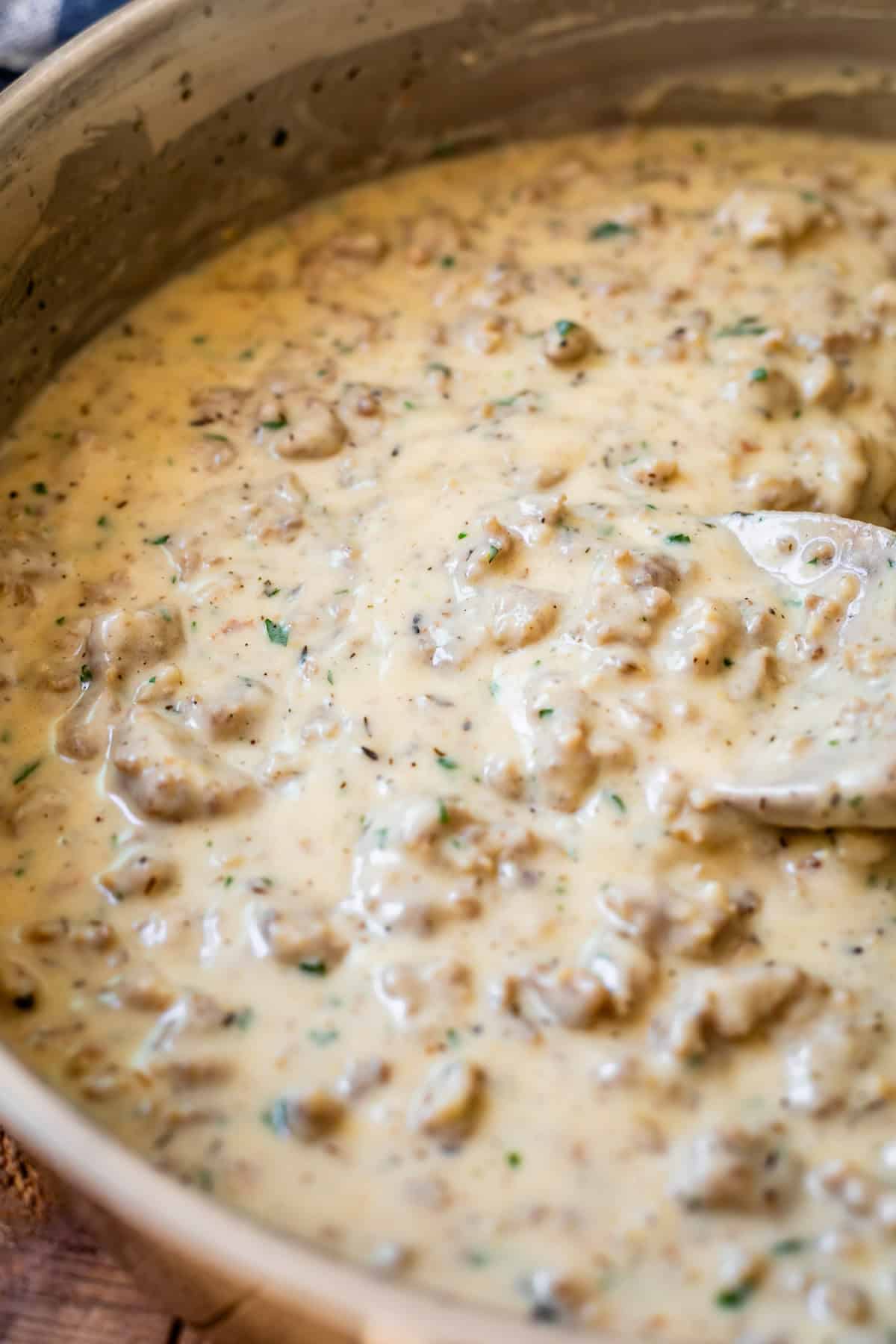 creamy sausage gravy being stirred by a wooden spoon in a metal pan.