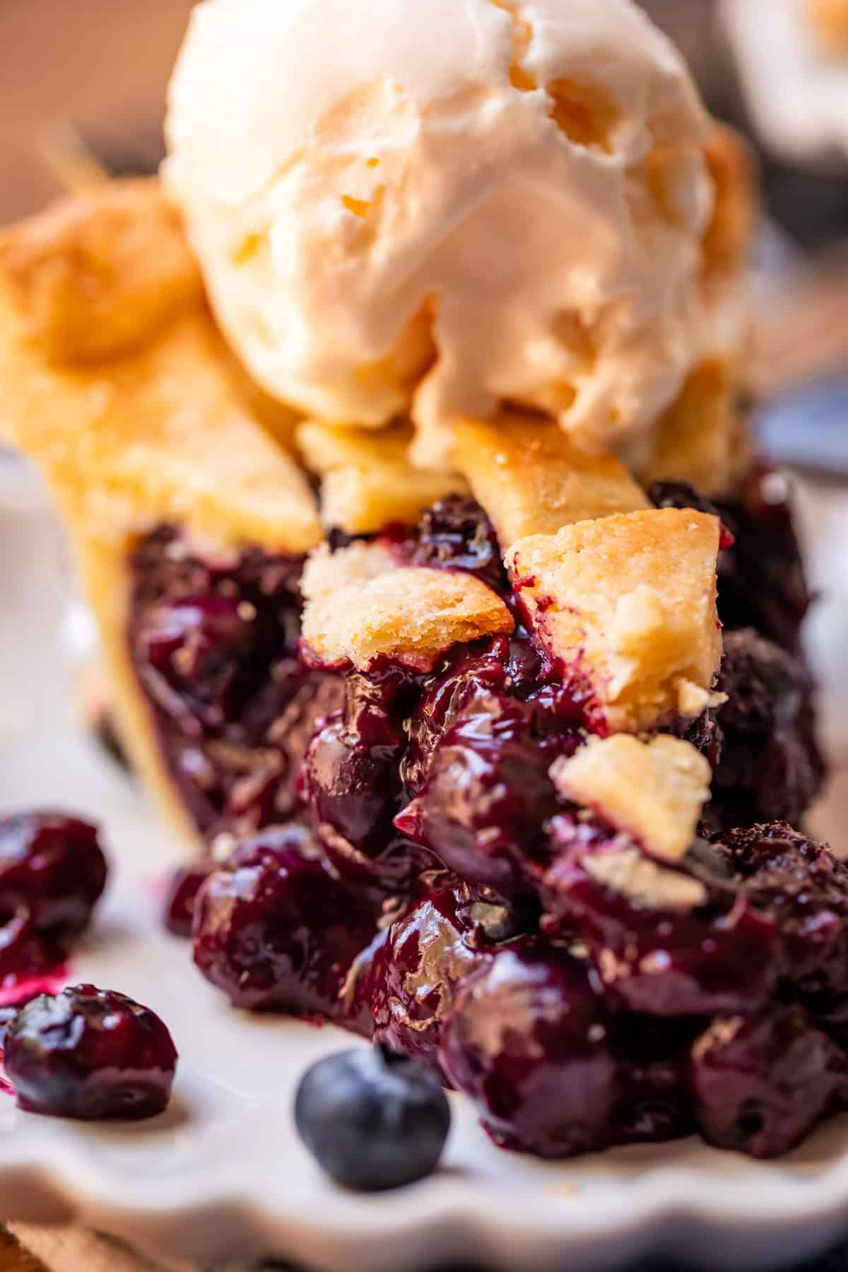 close up photo of the front of a slice of blueberry pie with ice cream on top.