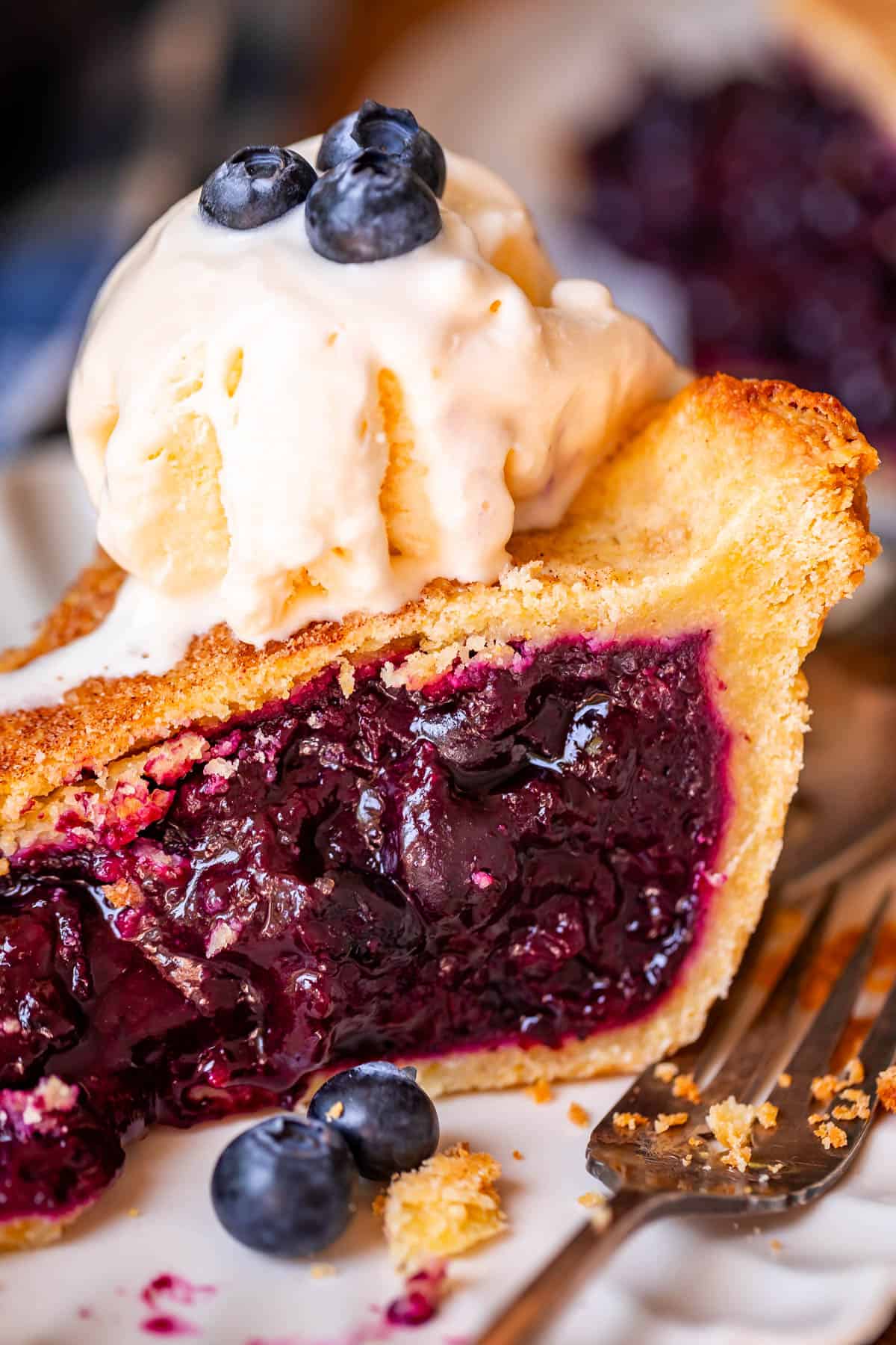 Slice Blueberry pie from the side with ice cream on top.