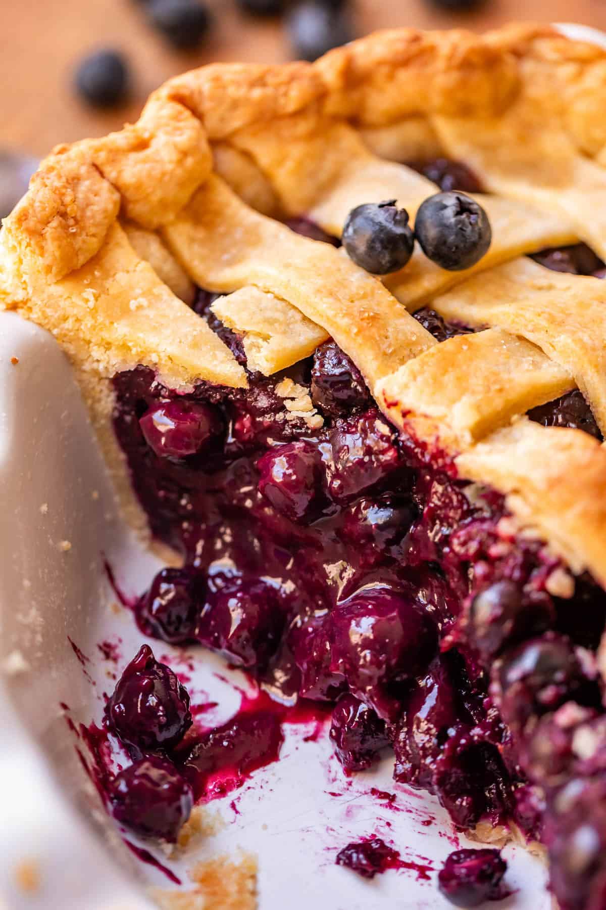 Blueberry pie in a pie dish with a slice removed and berries on top.