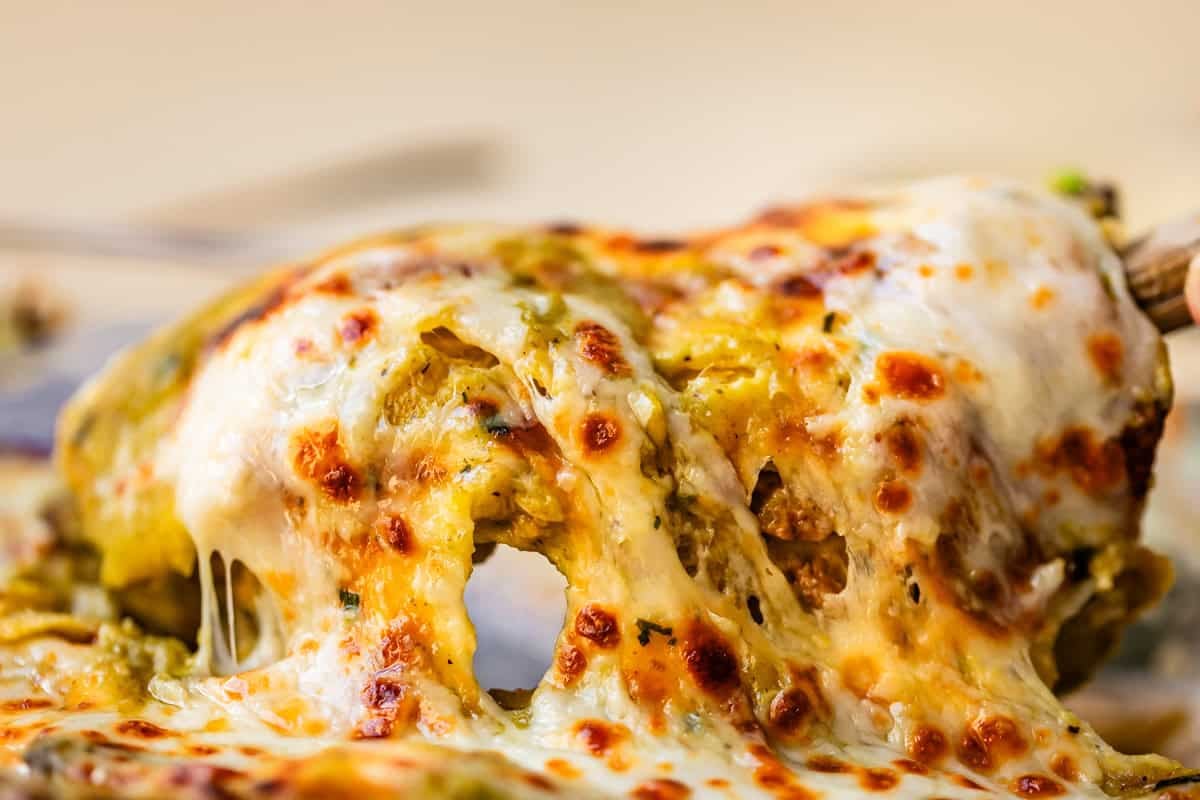 metal spatula lifting up an enchilada to serve showing all the delicious cheese stretch.
