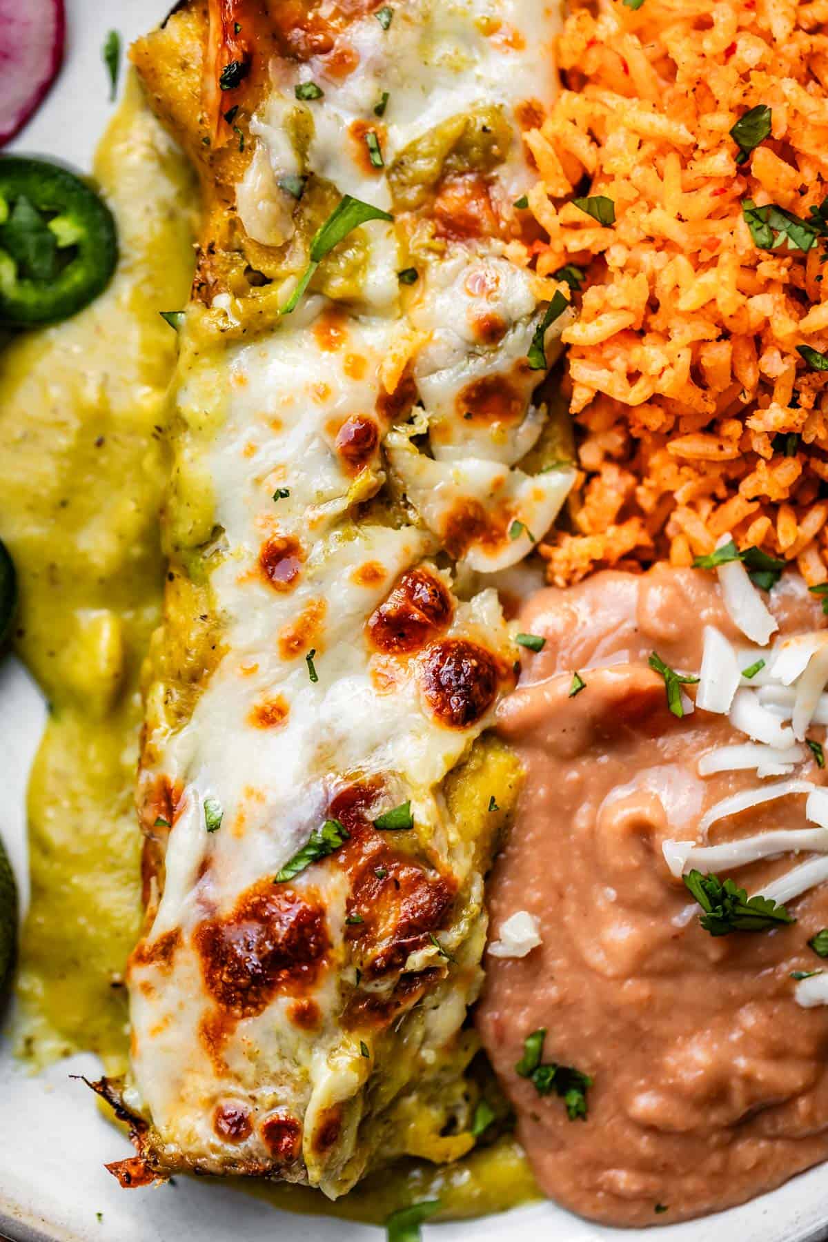 close up of rice, beans, and chicken enchiladas with jalapeno, lime, and avocado garnish.
