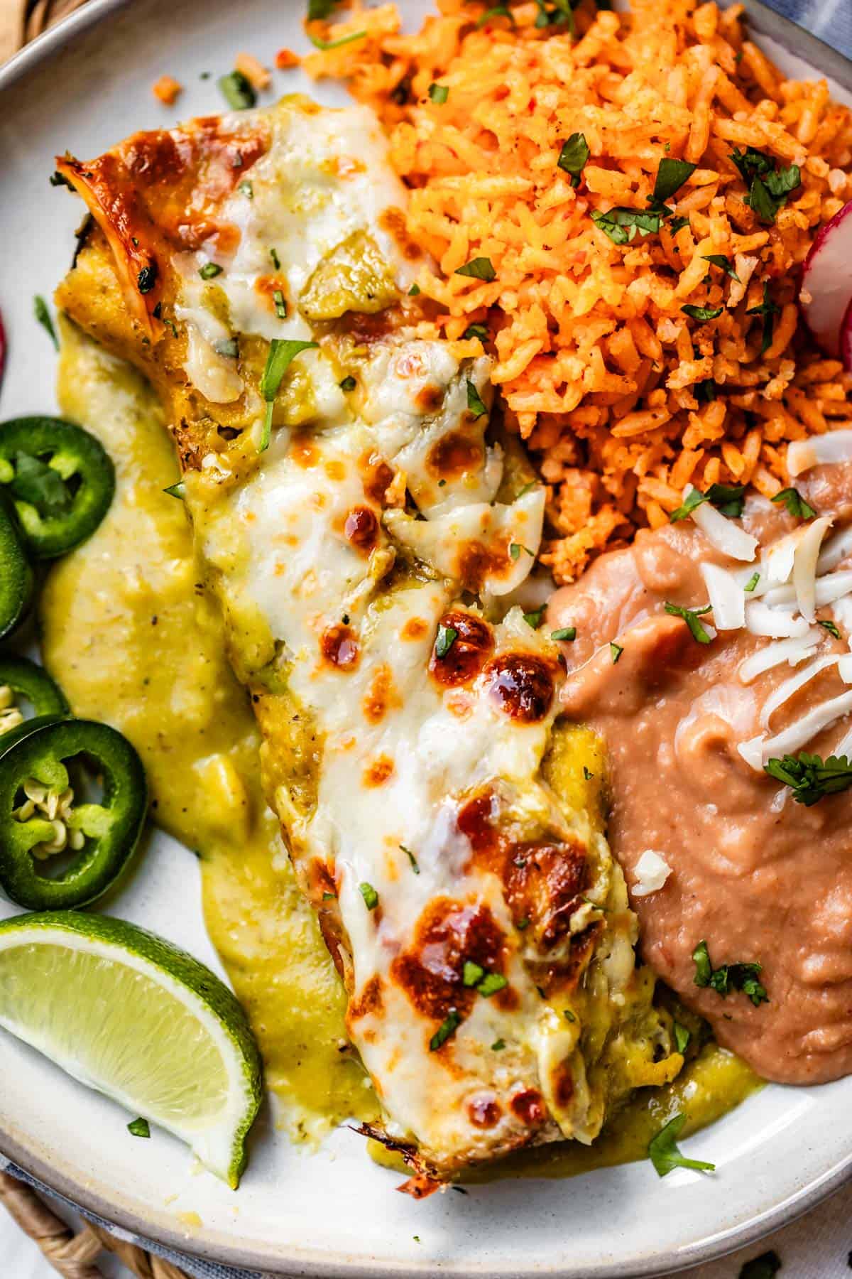 a plate filled with rice, beans, and chicken enchiladas with jalapeno, lime, and avocado garnish.