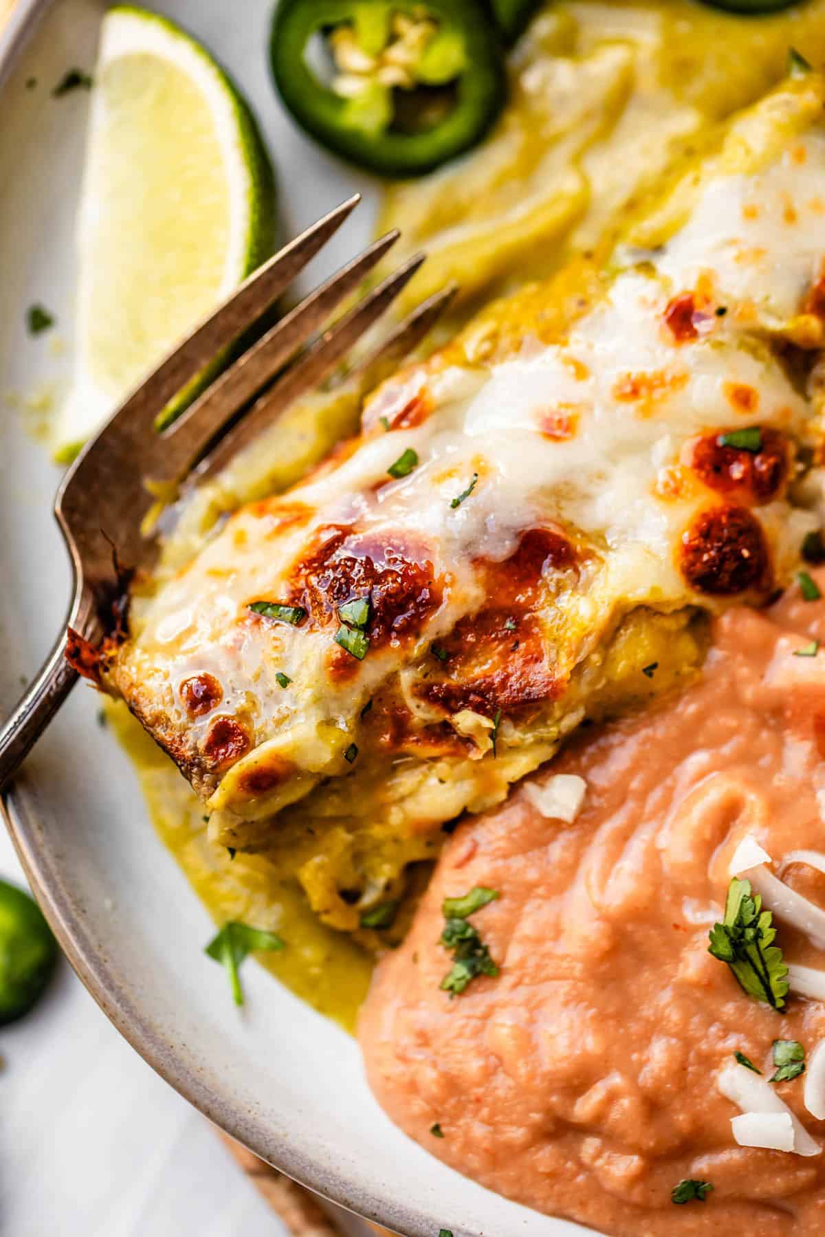 a plate of chicken enchiladas in green sauce on a plate with refried beans and a fork.