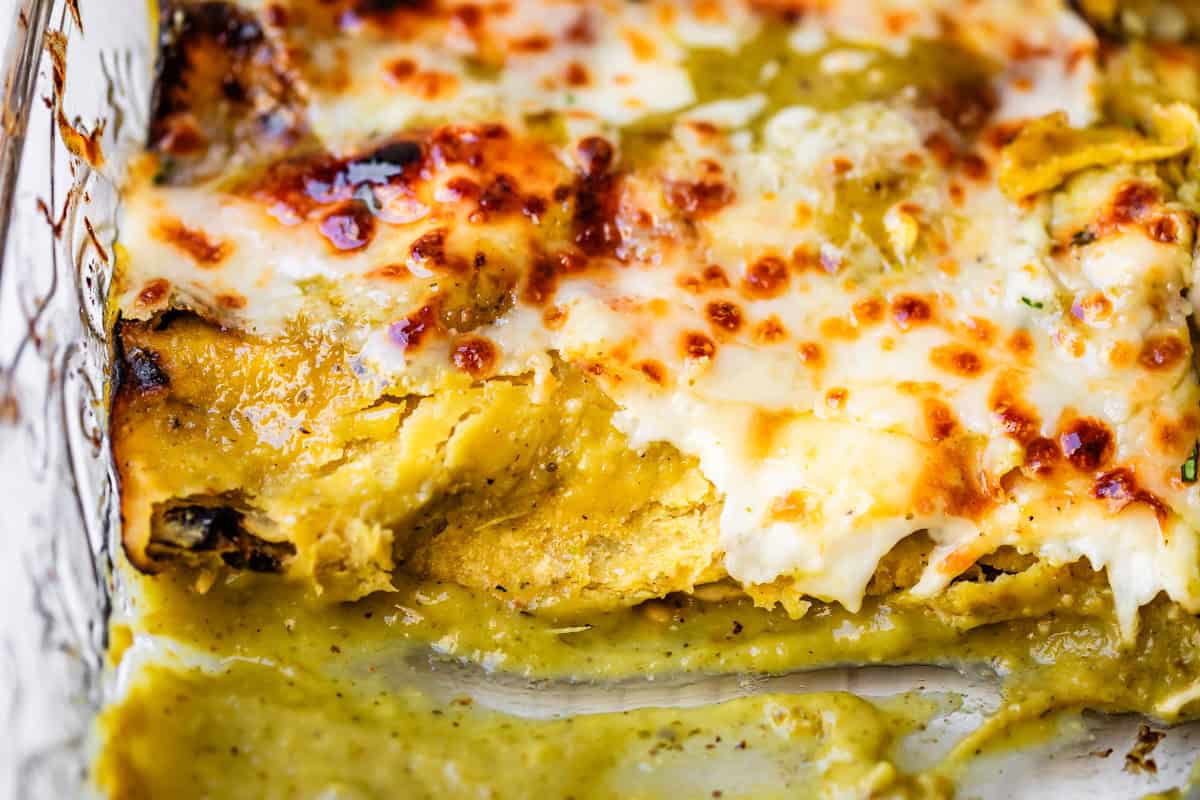 looking horizontally at a glass casserole dish of green sauce chicken enchiladas with some missing.