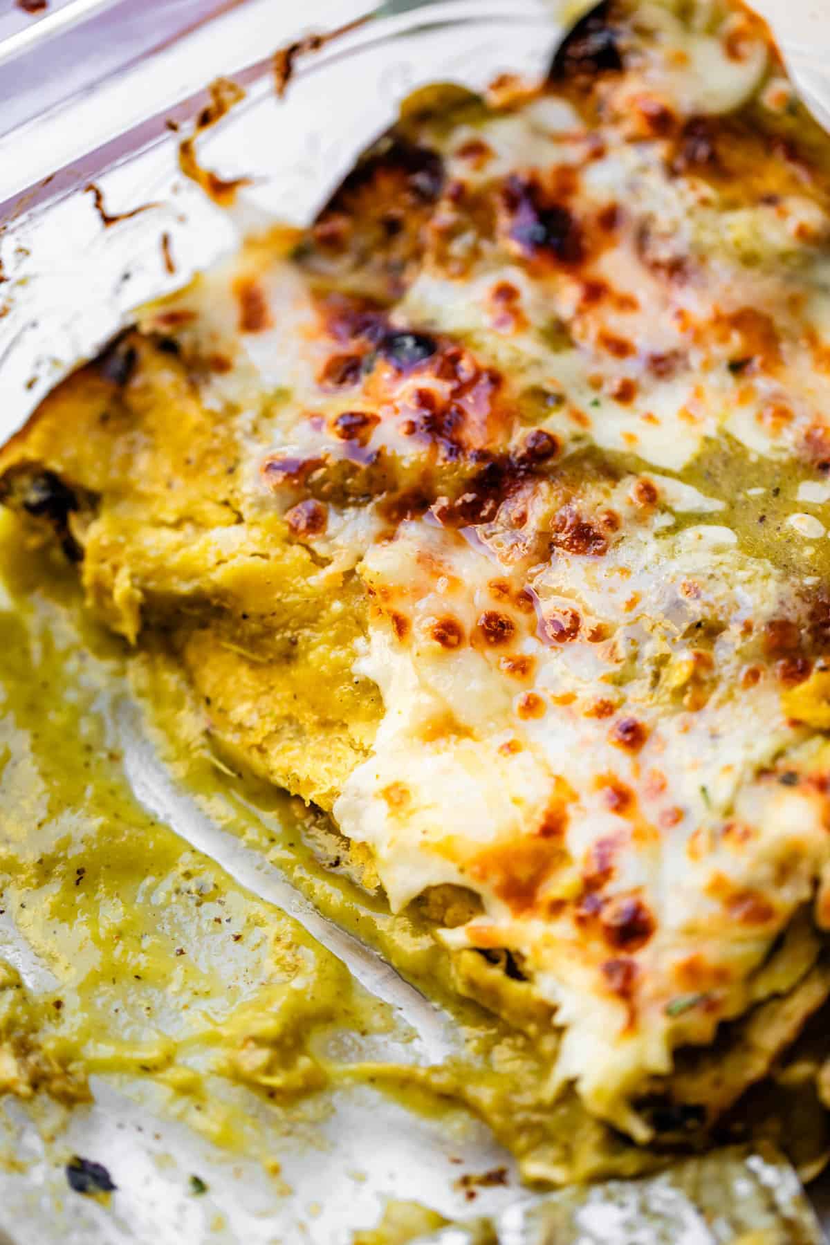 a glass casserole dish of green sauce chicken enchiladas with some missing.
