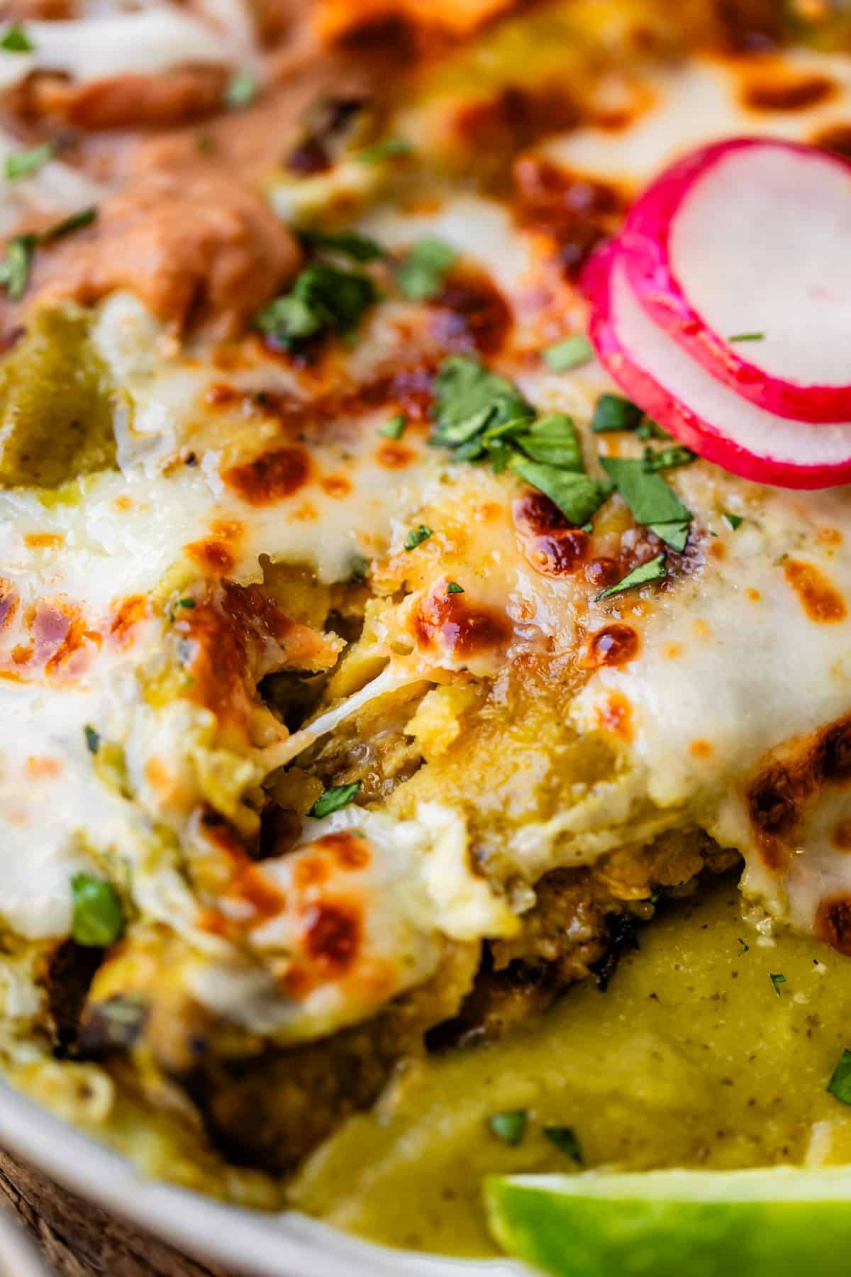 close up of green chicken enchiladas on a plate showing cheese stretch.