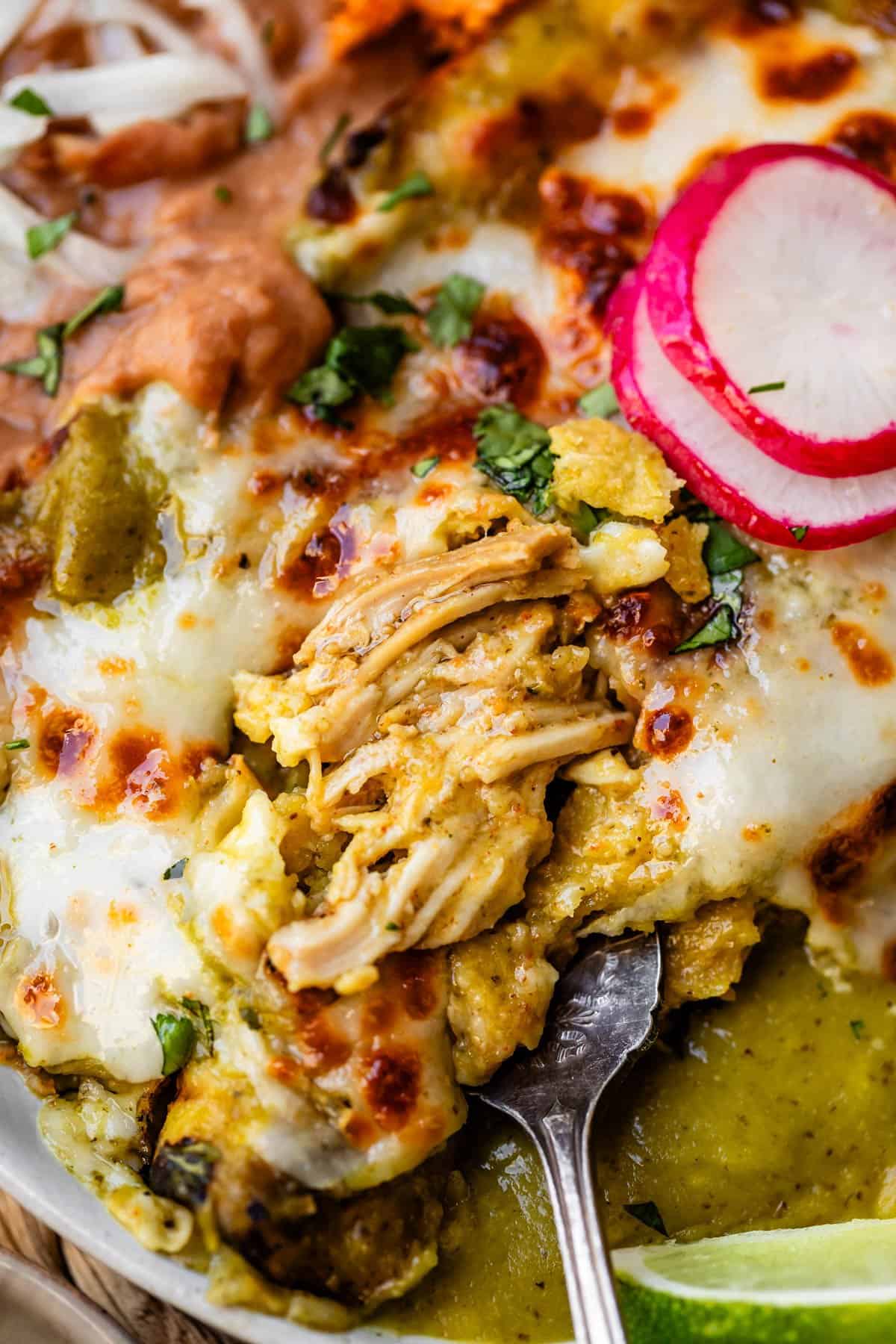 green enchiladas with a fork pulling out the chicken to show the insides.