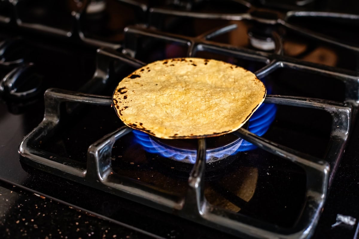 charred corn tortilla directly on burner over flame on a gas stove.