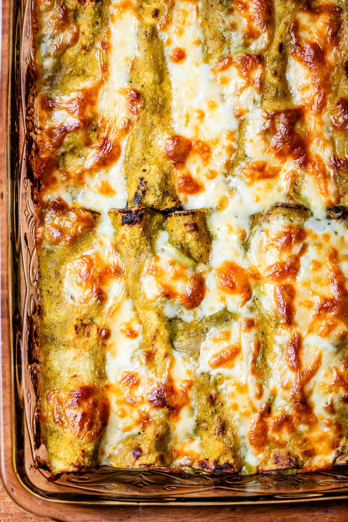 looking down at a glass casserole dish of baked green chicken enchiladas,