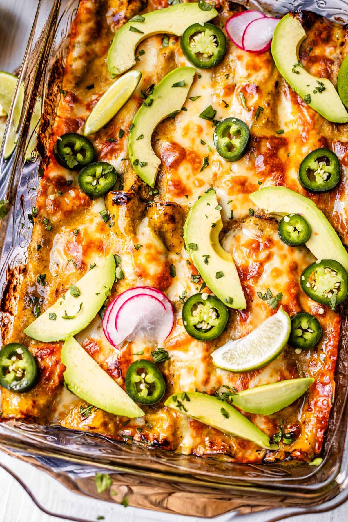 looking down at a glass casserole dish of baked enchiladas, topped with avocado, radish, jalapeno, etc.