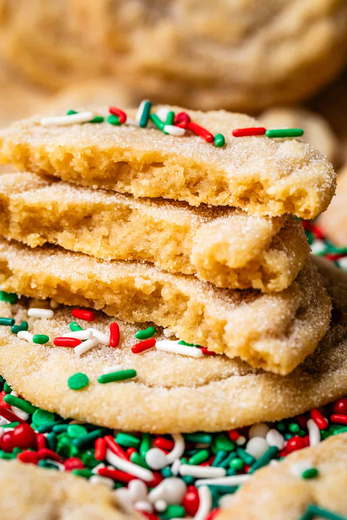 three halved no roll sugar cookies stacked with Christmas color sprinkles on top.