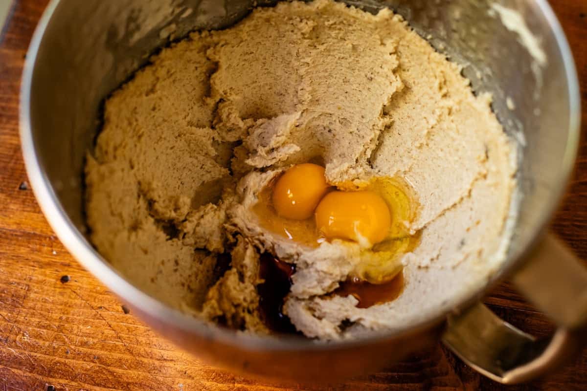 eggs added to creamed butter and sugars in a metal mixing bowl.
