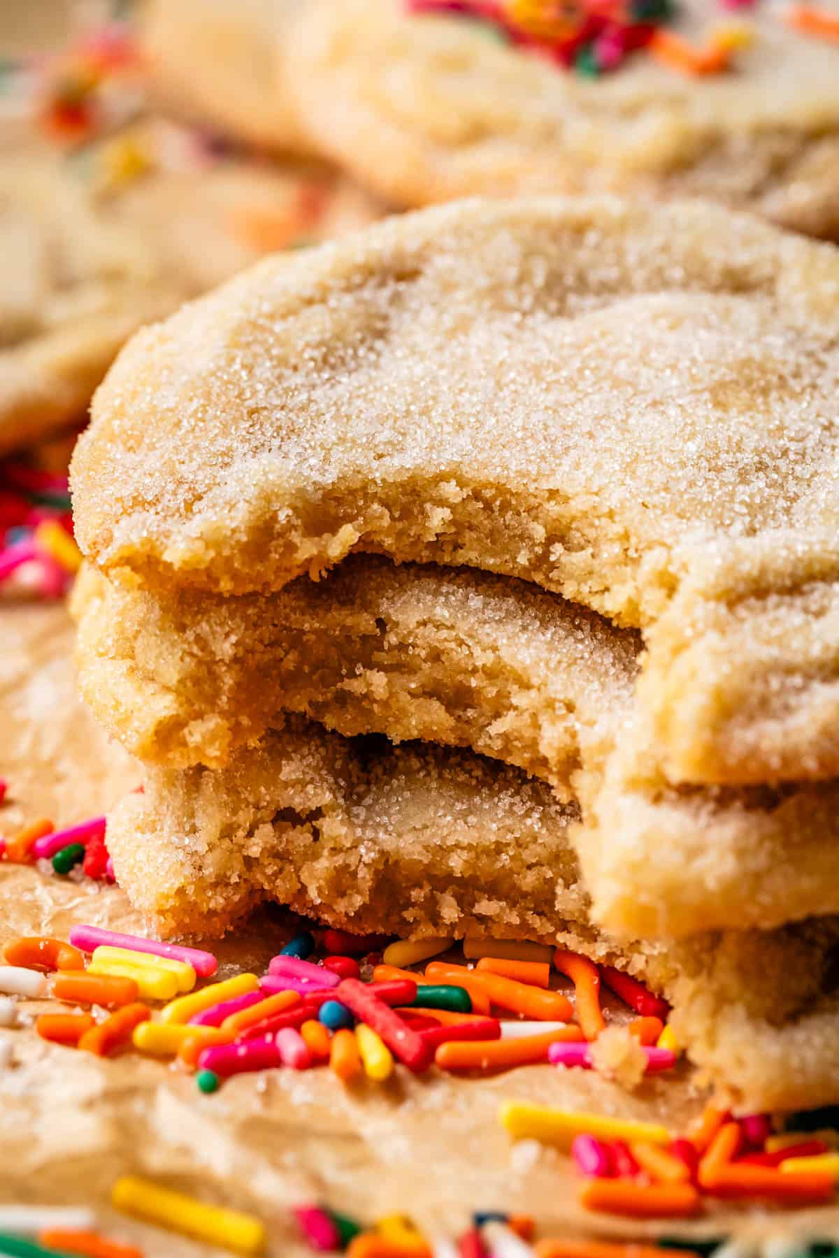 three stacked sugar cookies with a bite taken from them sitting on top of sprinkles.