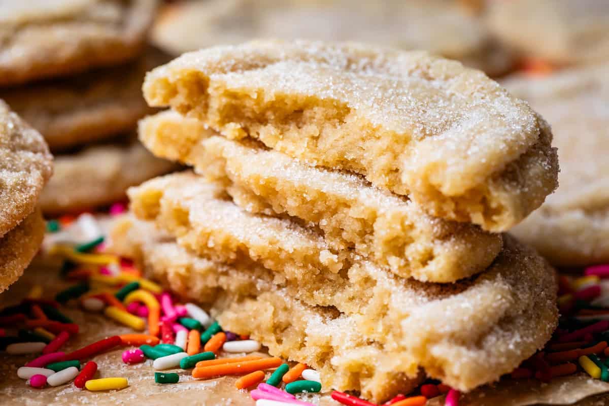 four stacked halves of no roll sugar cookies sitting on top of sprinkles on parchment paper.