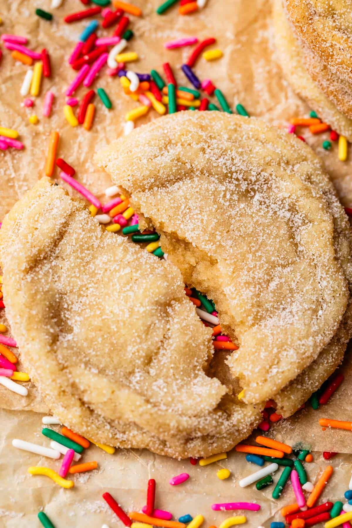 a drop sugar cookie in two pieces on top of sprinkles on parchment paper.