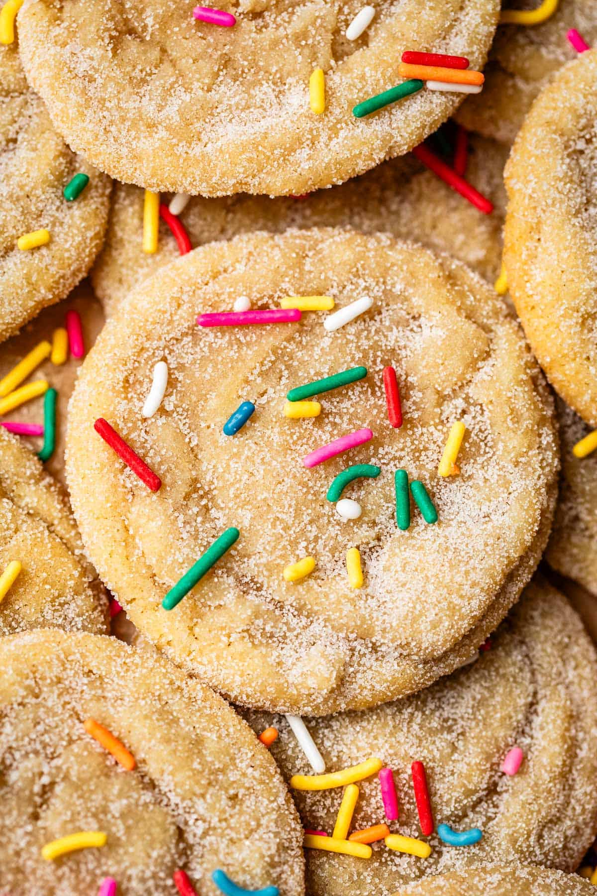 loose pile of no roll sugar cookies all topped with rainbow colored sprinkles.