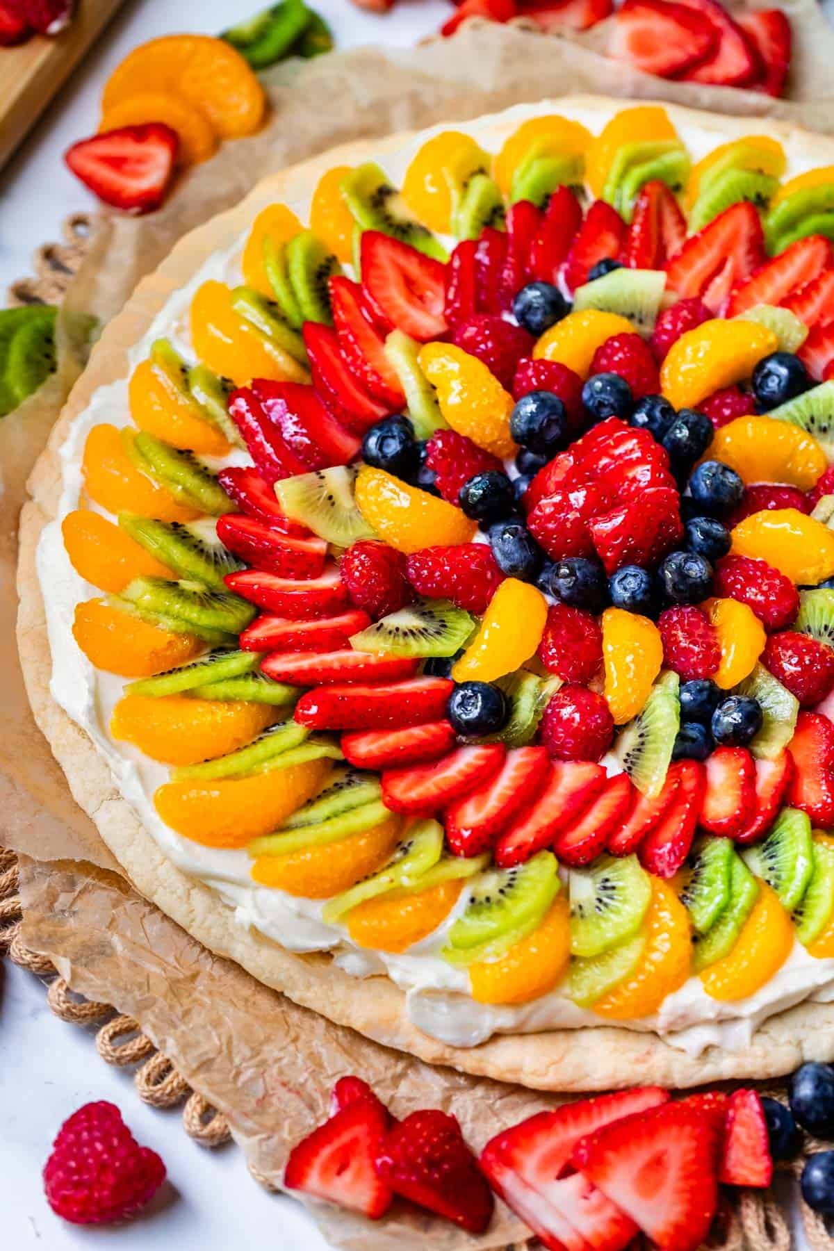 whole fruit pizza beautifully topped with oranges, kiwi, strawberries, blueberries, and more.