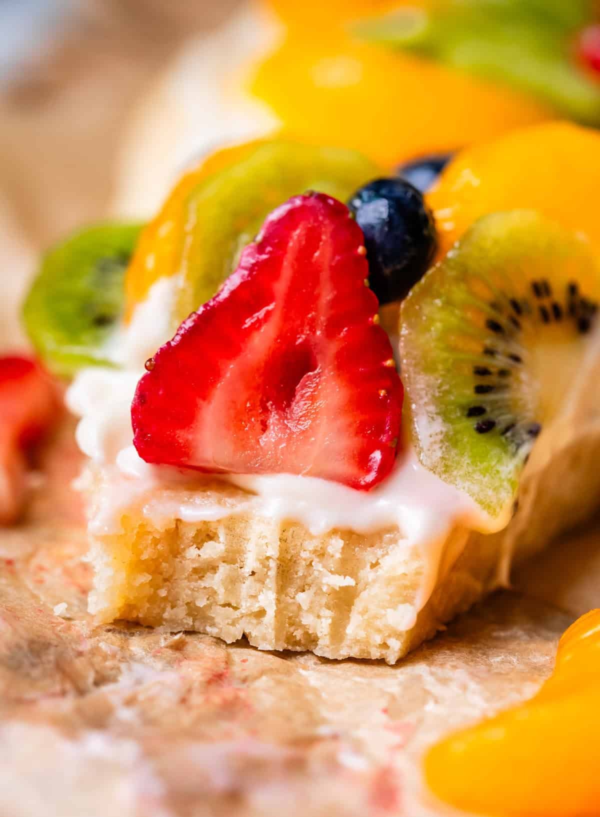 piece of fruit pizza with a bite taken from it showing all the layers.