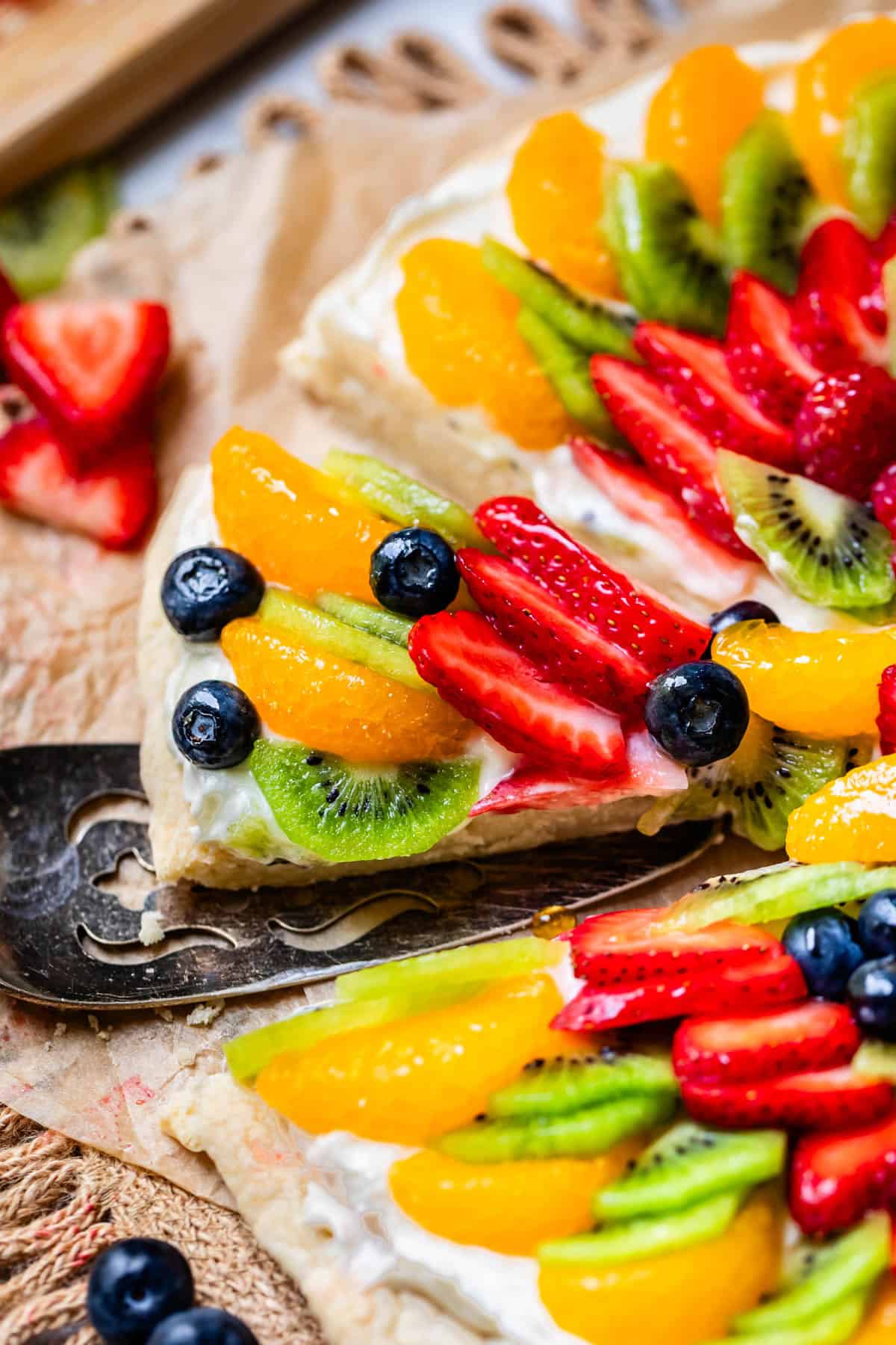 serving spatula lifting up a slice of fruit pizza from the whole pizza.