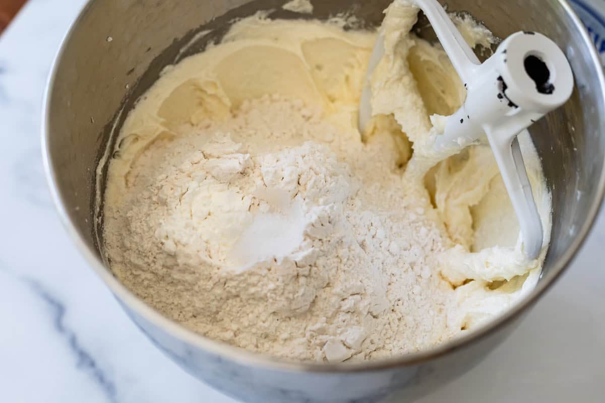flour added to the top of the butter and cream cheese mixture in the metal mixing bowl.