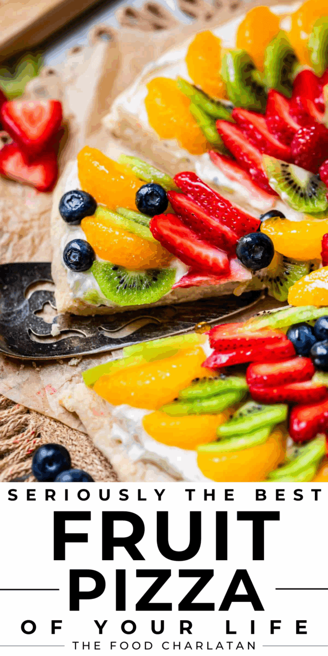 Pie server lifting a slice of fruit pizza from parchment paper.