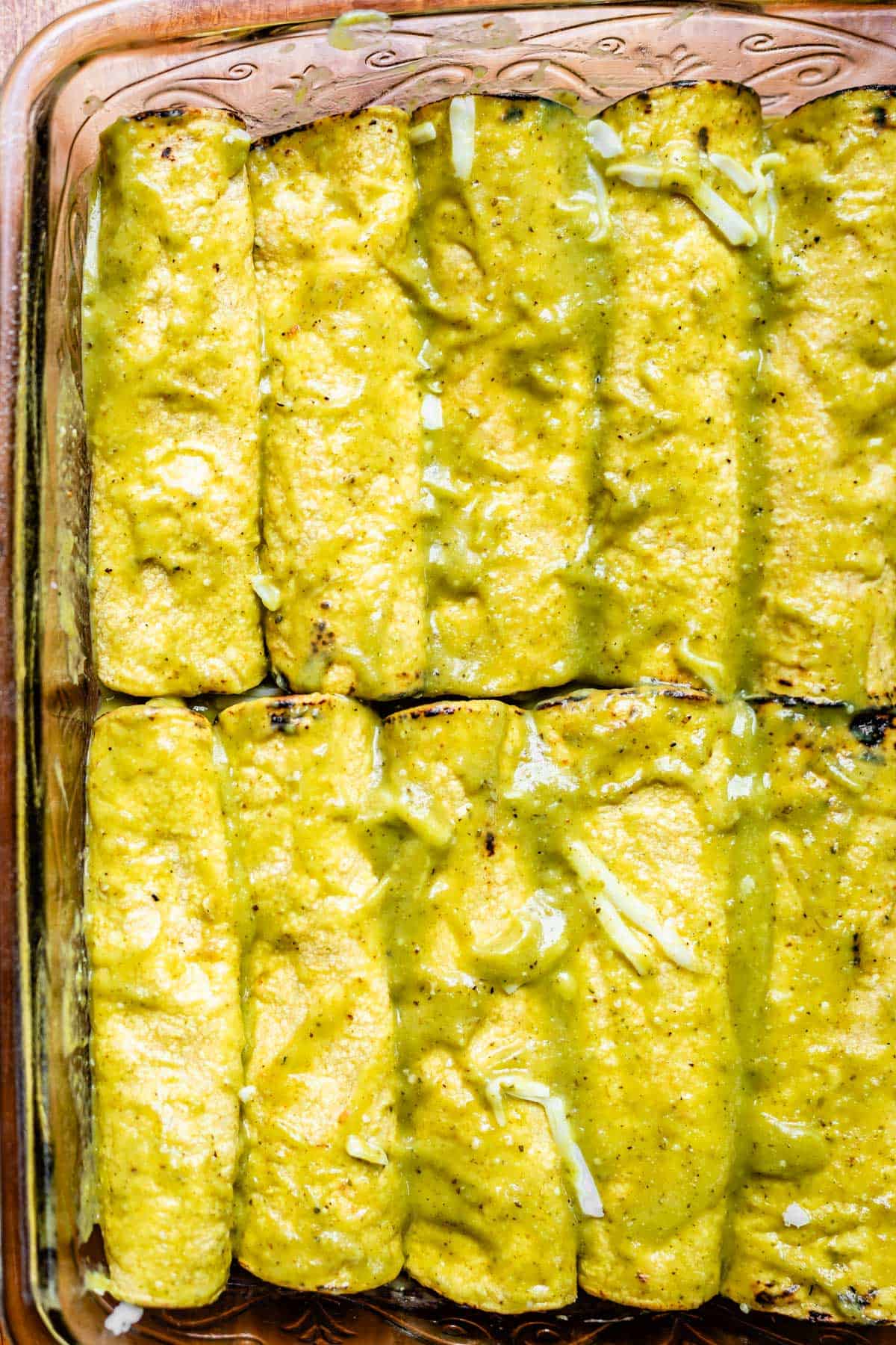 a glass casserole dish with enchiladas coated in green enchilada sauce.