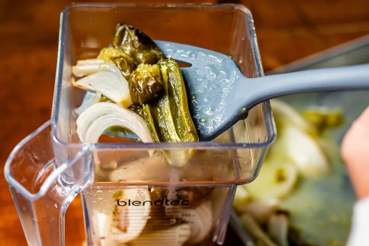 spatula holding roasted onion and jalapenos adding them to a blender.