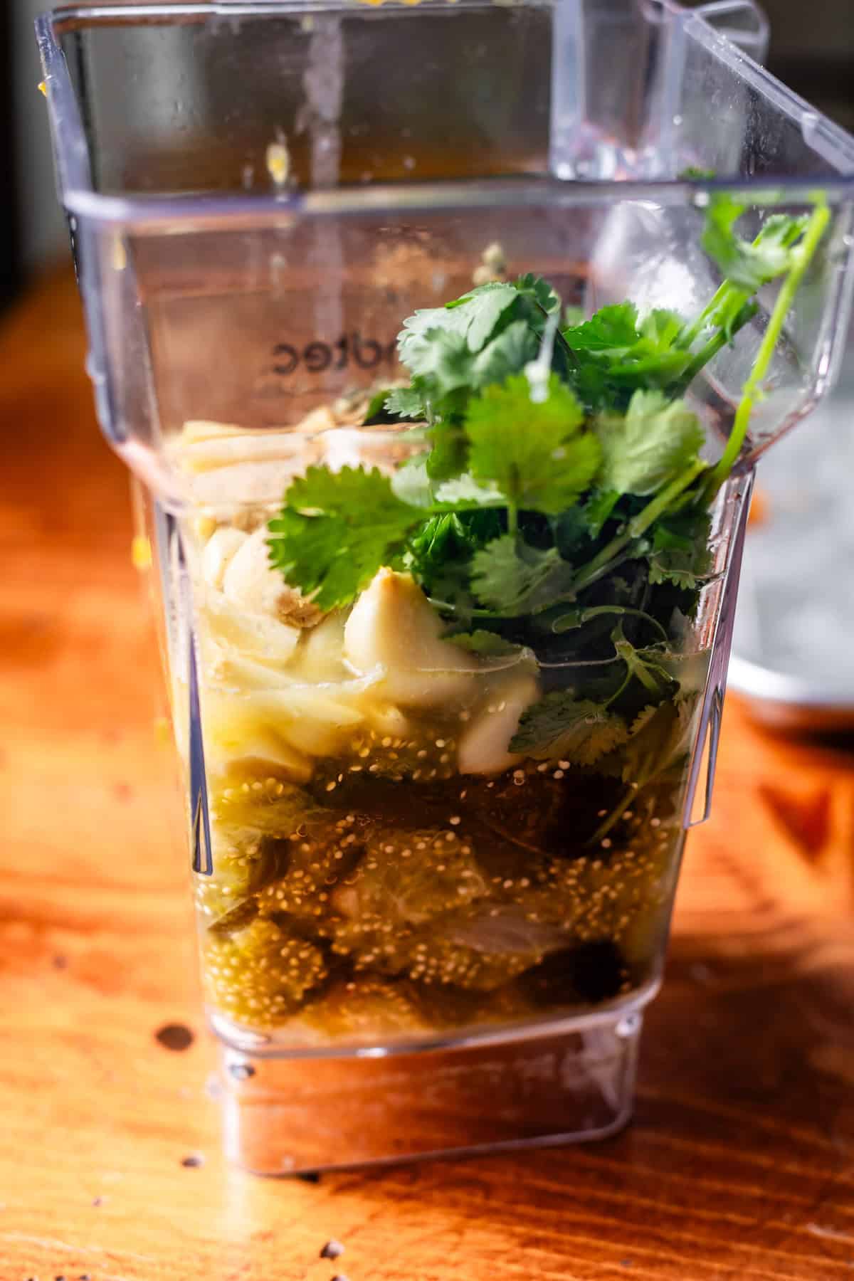 side view of blender with all the green enchilada sauce ingredients ready to be blended.