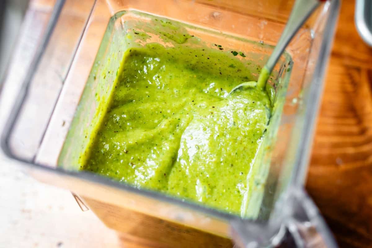 a blender with a metal spoon inside scooping up some green enchilada sauce.