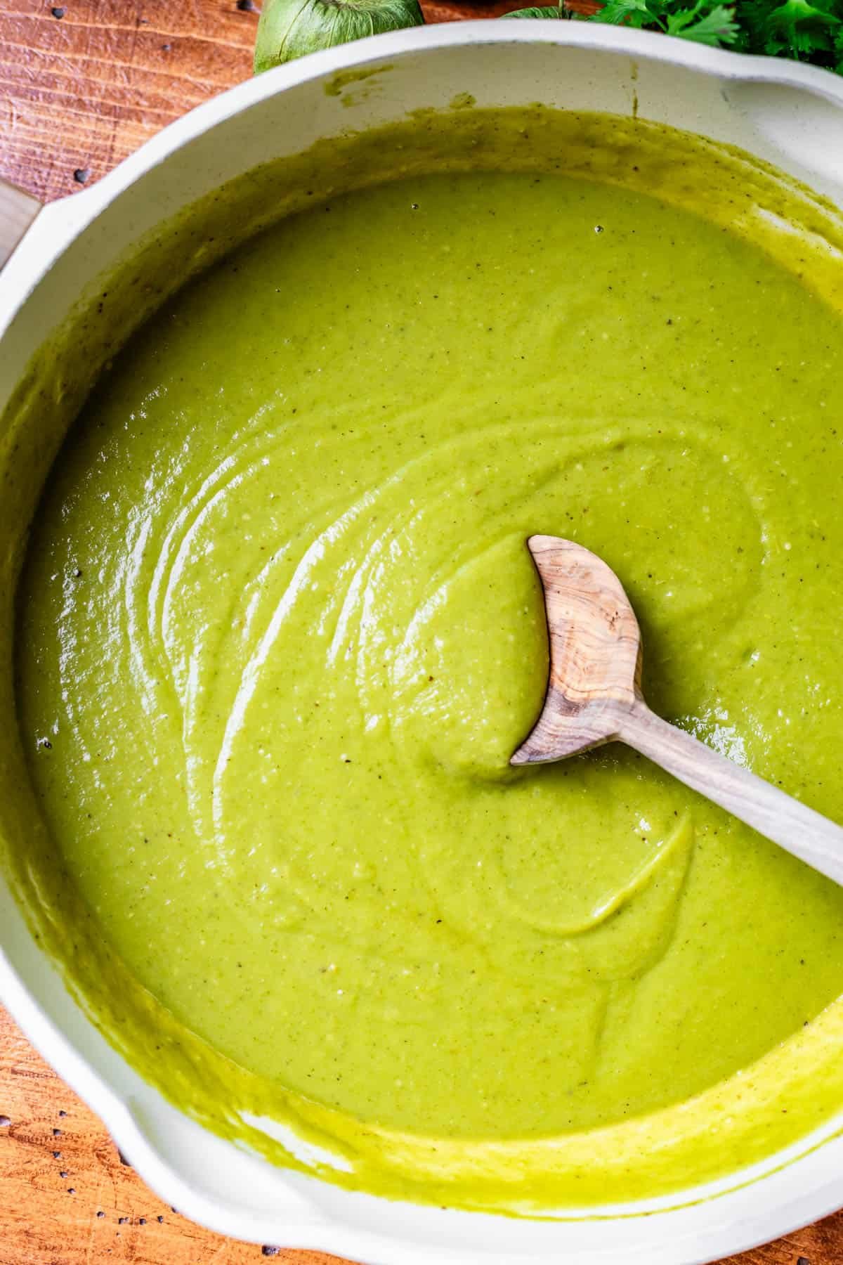a large skillet filled with green enchilada sauce with a wooden spoon stirring it.