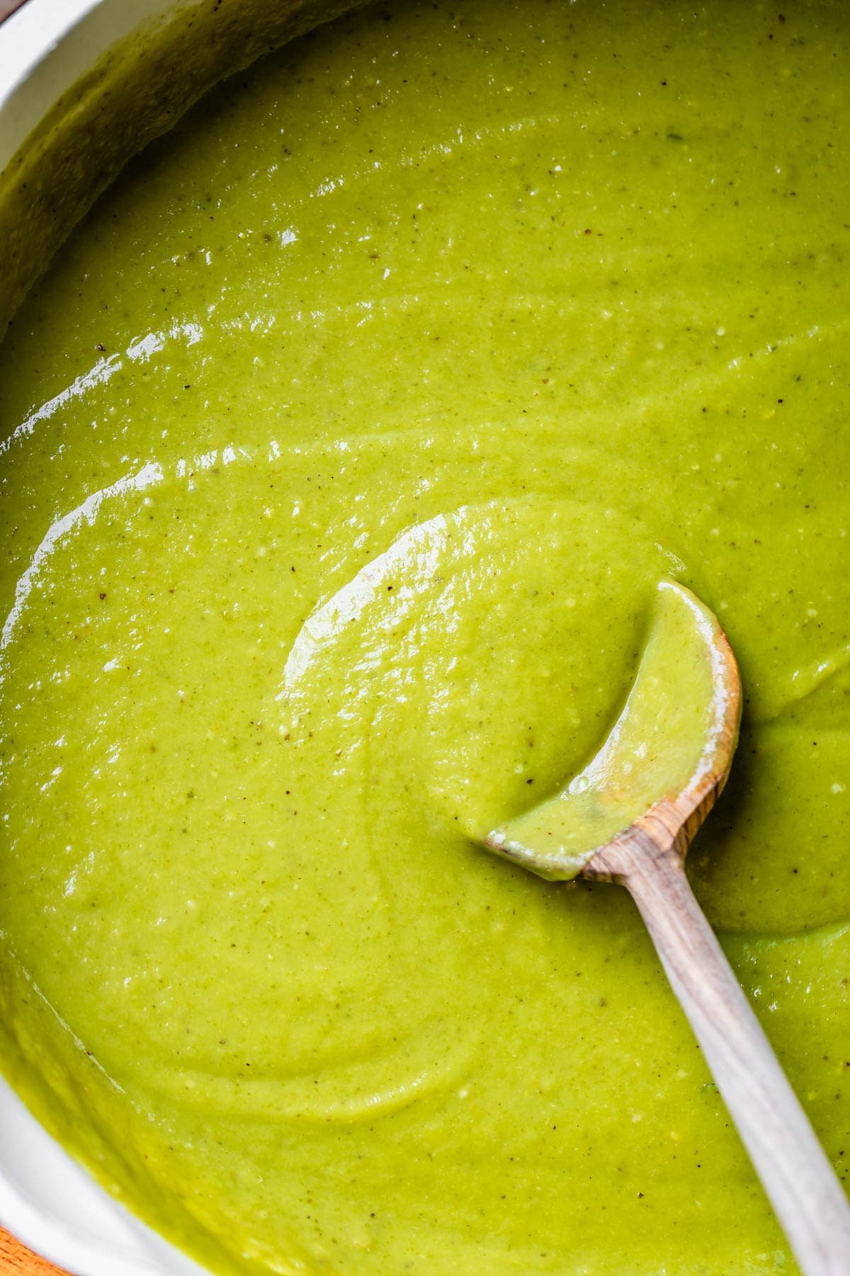 a large skillet filled with green enchilada sauce with a wooden spoon stirring it.