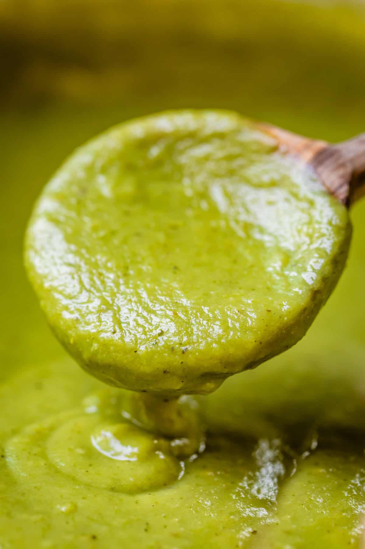 a wooden spoon pouring some green enchilada sauce back into more sauce.