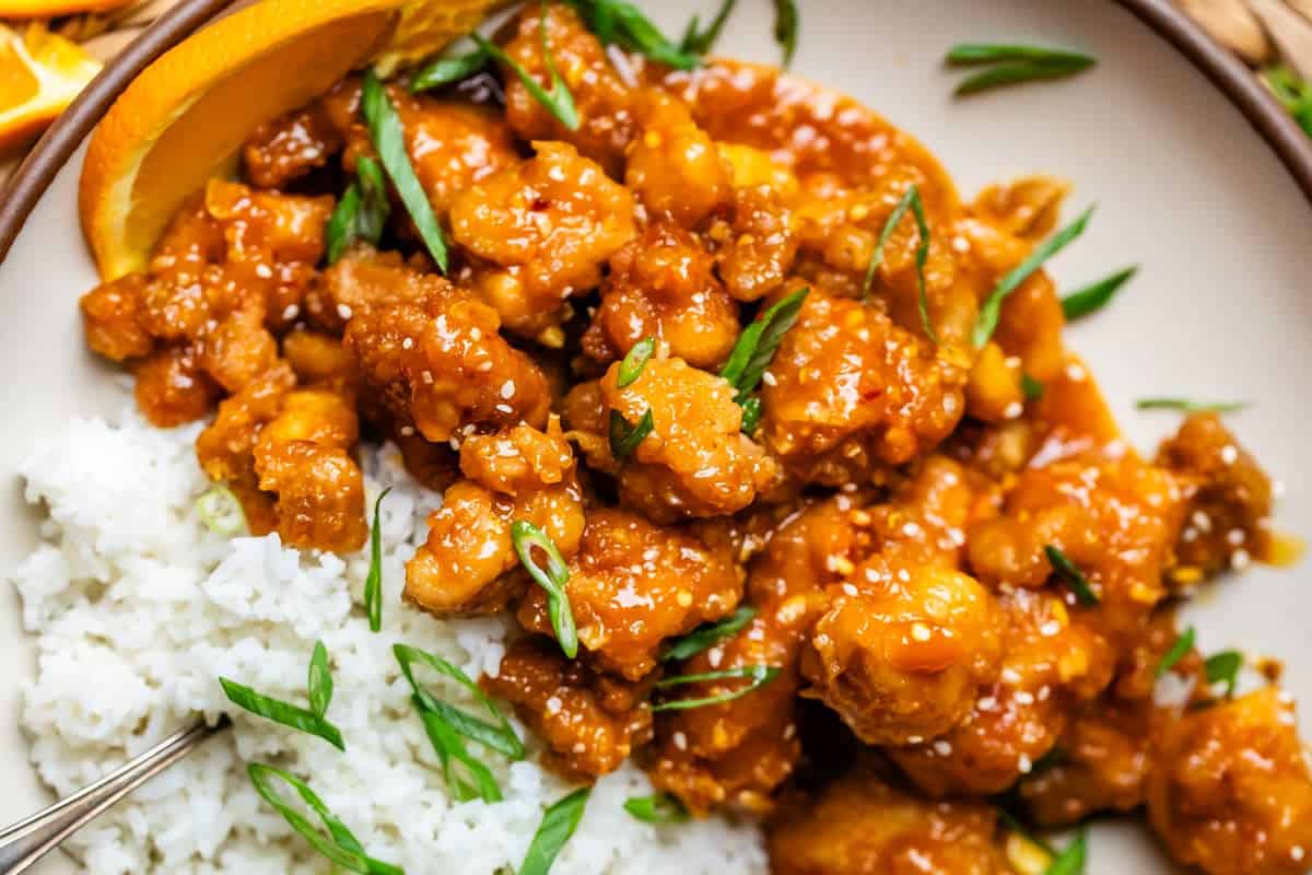 white rice and crispy orange chicken with green onion garnish on dinner plate.