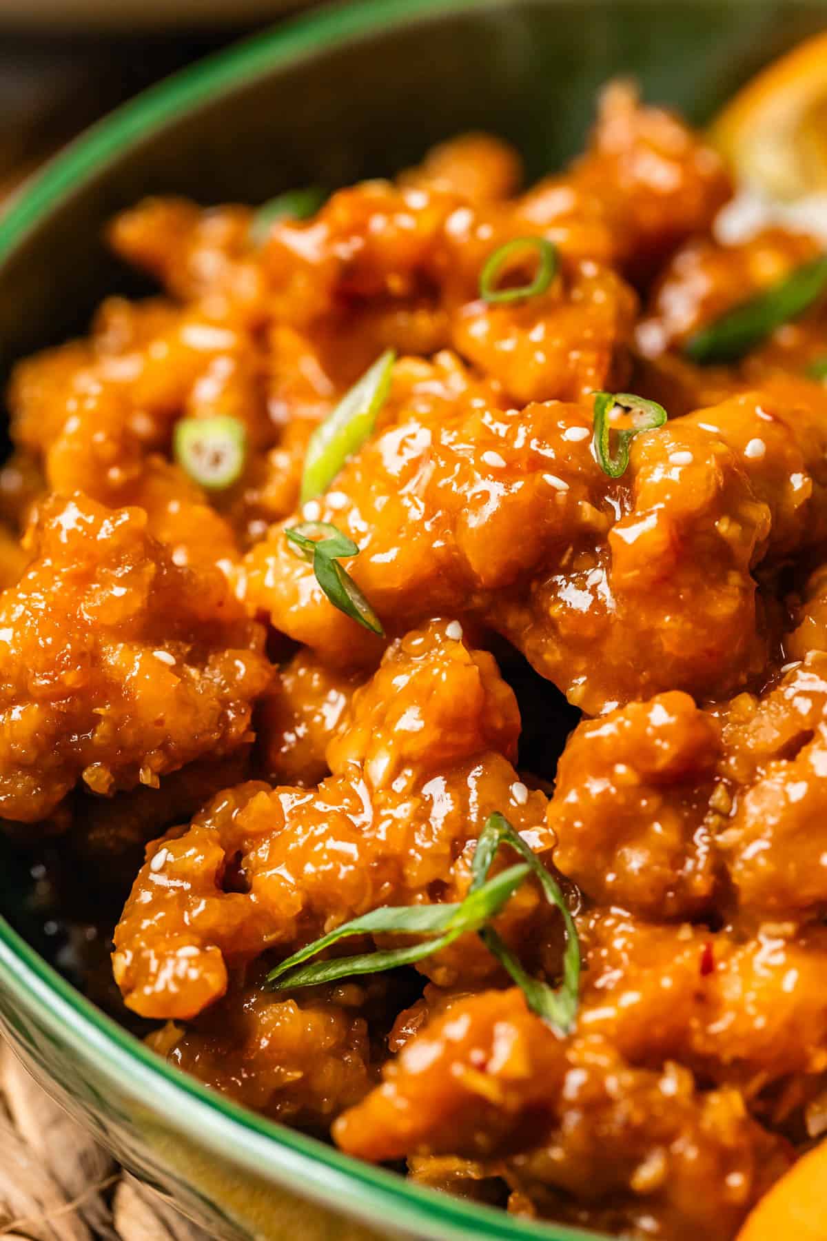 close up of crispy orange chicken with green onion garnish in ceramic bowl.