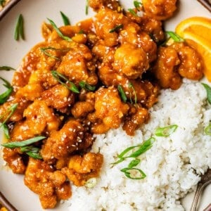 white rice and crispy orange chicken with green onion garnish on a dinner plate.