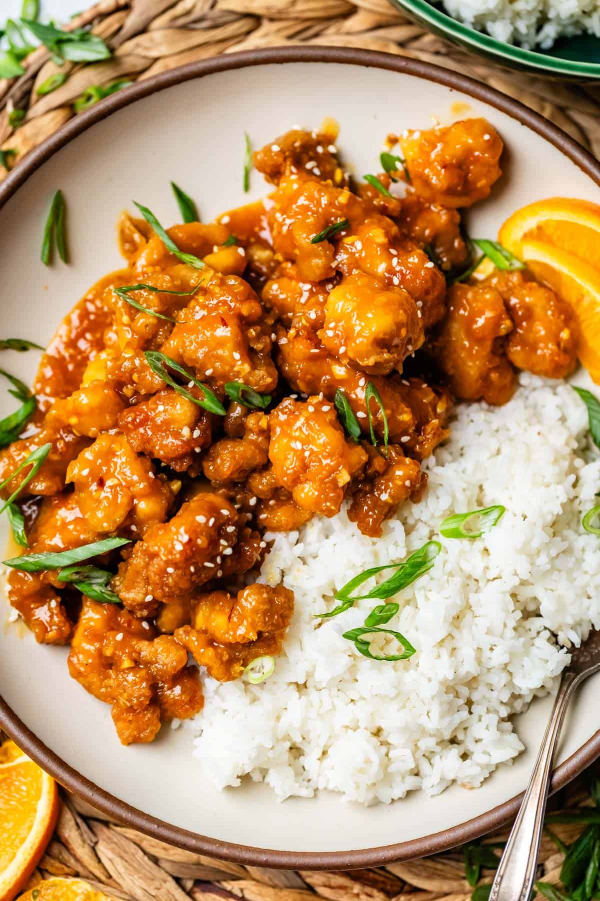 white rice and crispy orange chicken with green onion garnish on a dinner plate.
