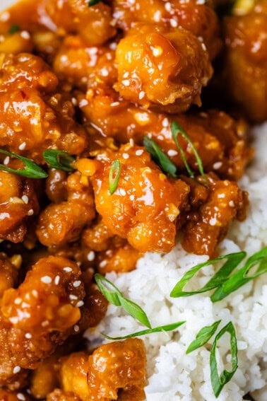 close up of white rice and crispy orange chicken with green onion garnish.