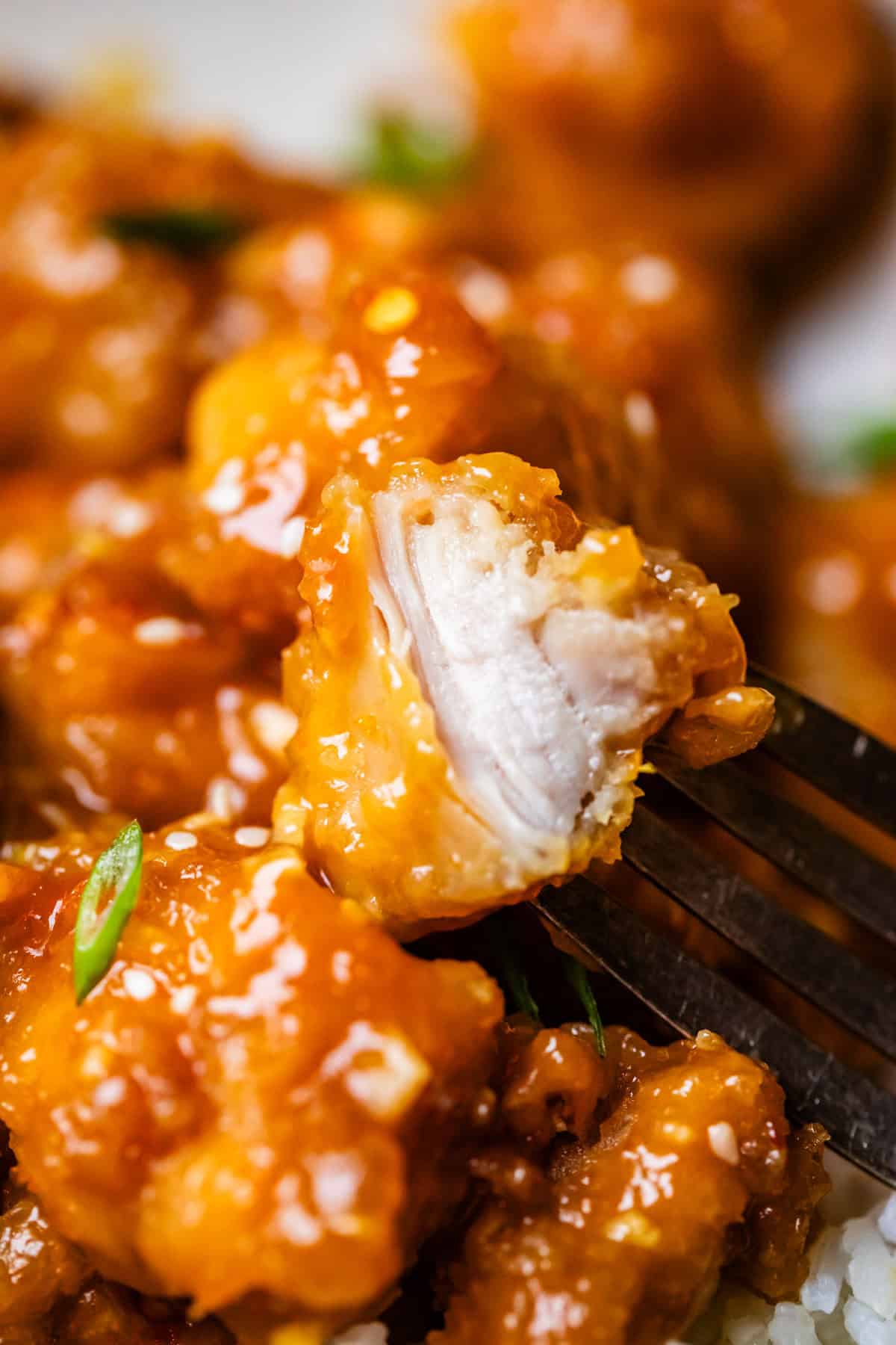 close up of fork holding a piece of orange chicken showing the tender inside.