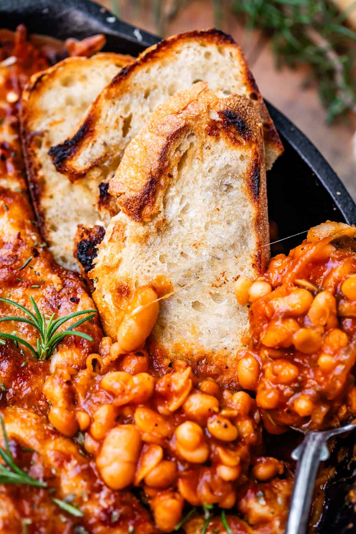 metal spoon and 3 sourdough slices stuck into a cast iron skillet of cheesy beans.