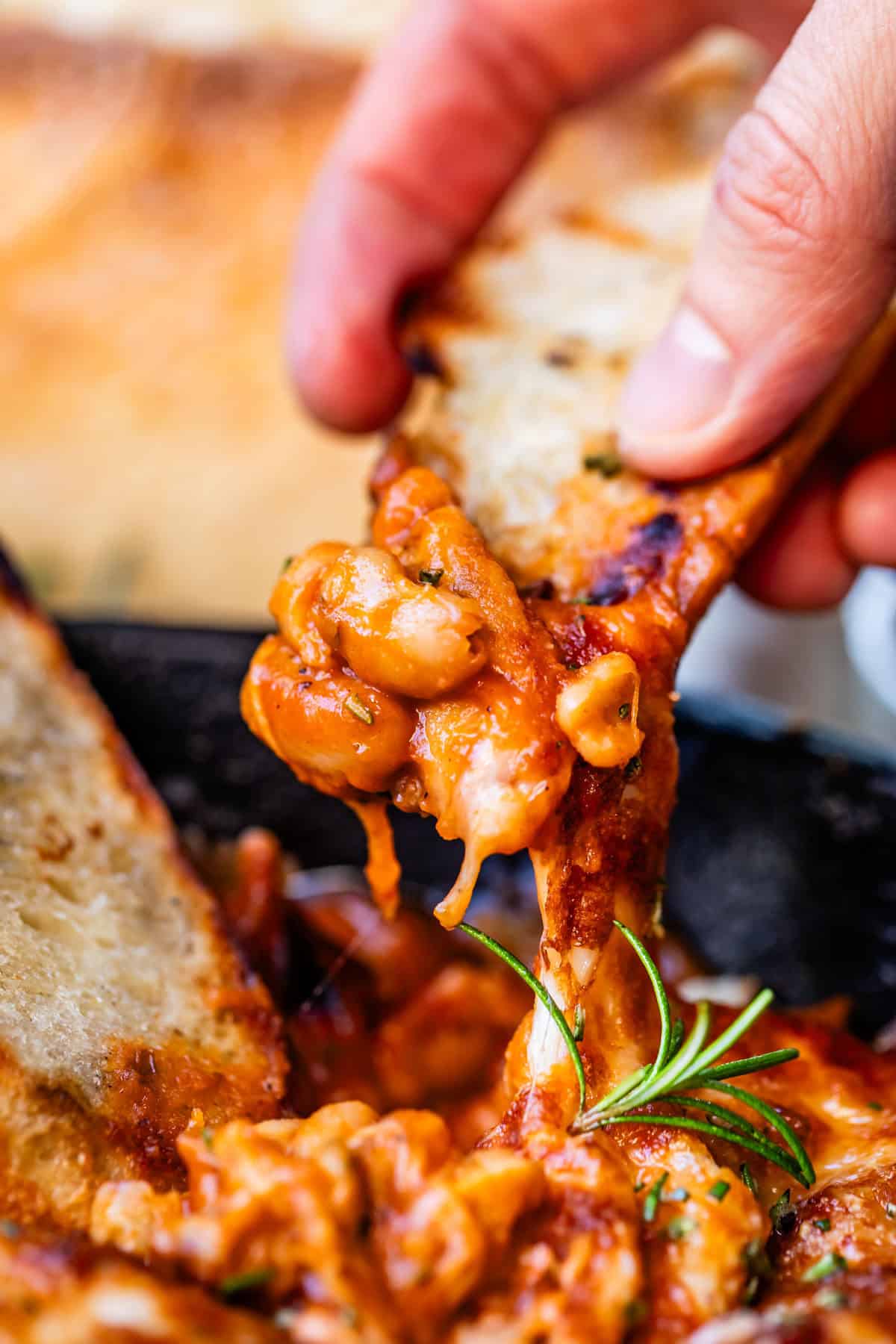 hand holding a piece of bread that has scooped up some cheesy bean bake.