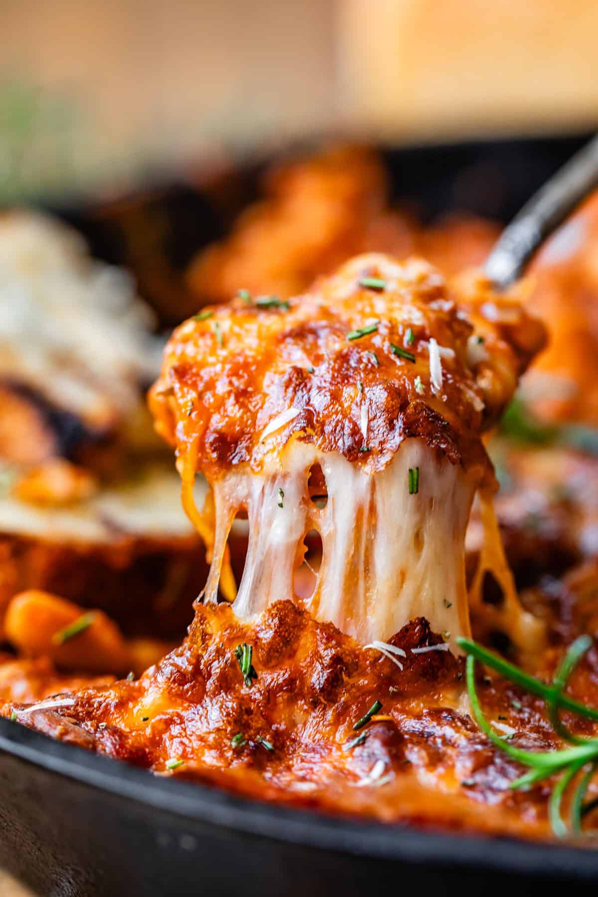 spoon pulling up white bean tomato bake with a long cheese stretch.